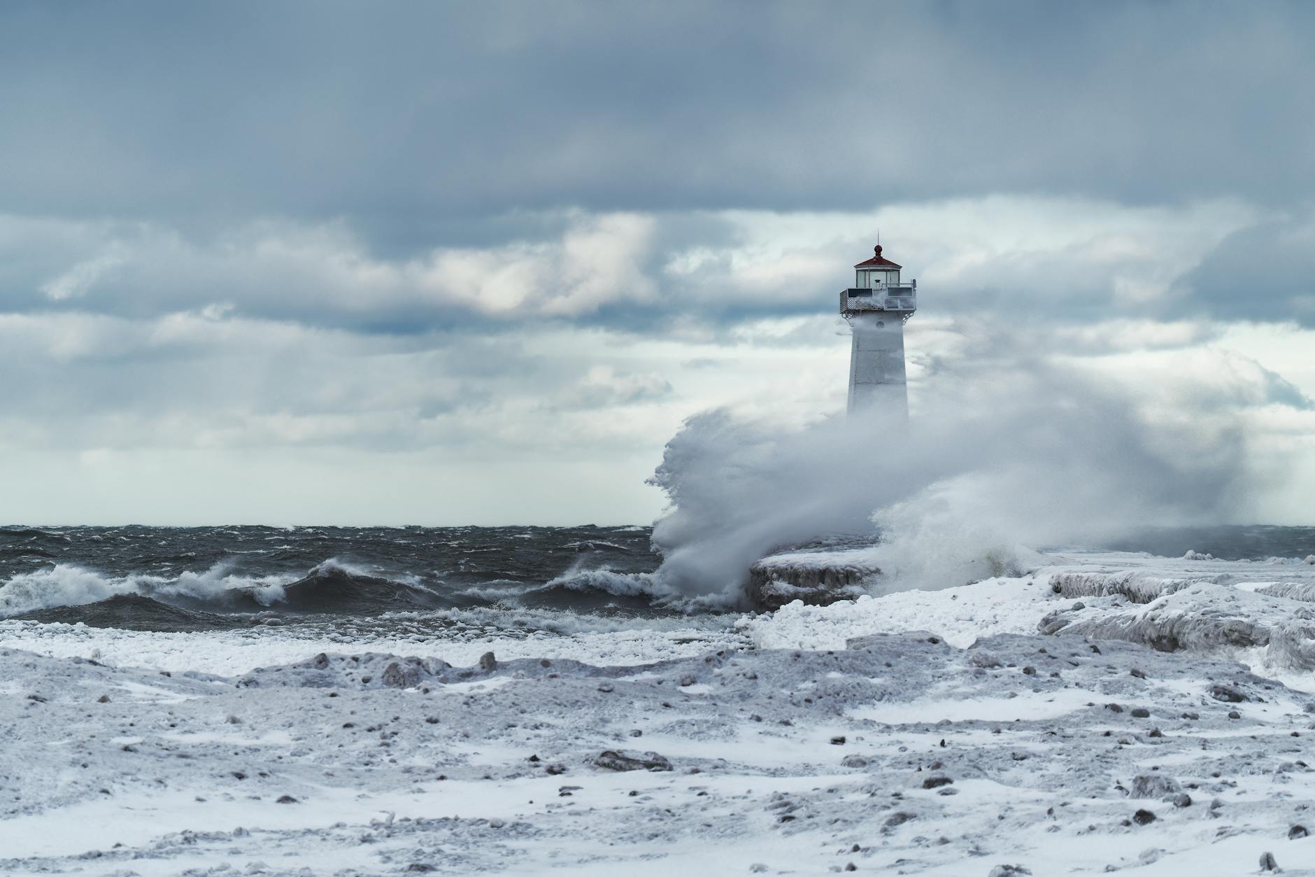 Dramatic winter scene with waves crashing at Sodus Point Lighthouse on snowy day.