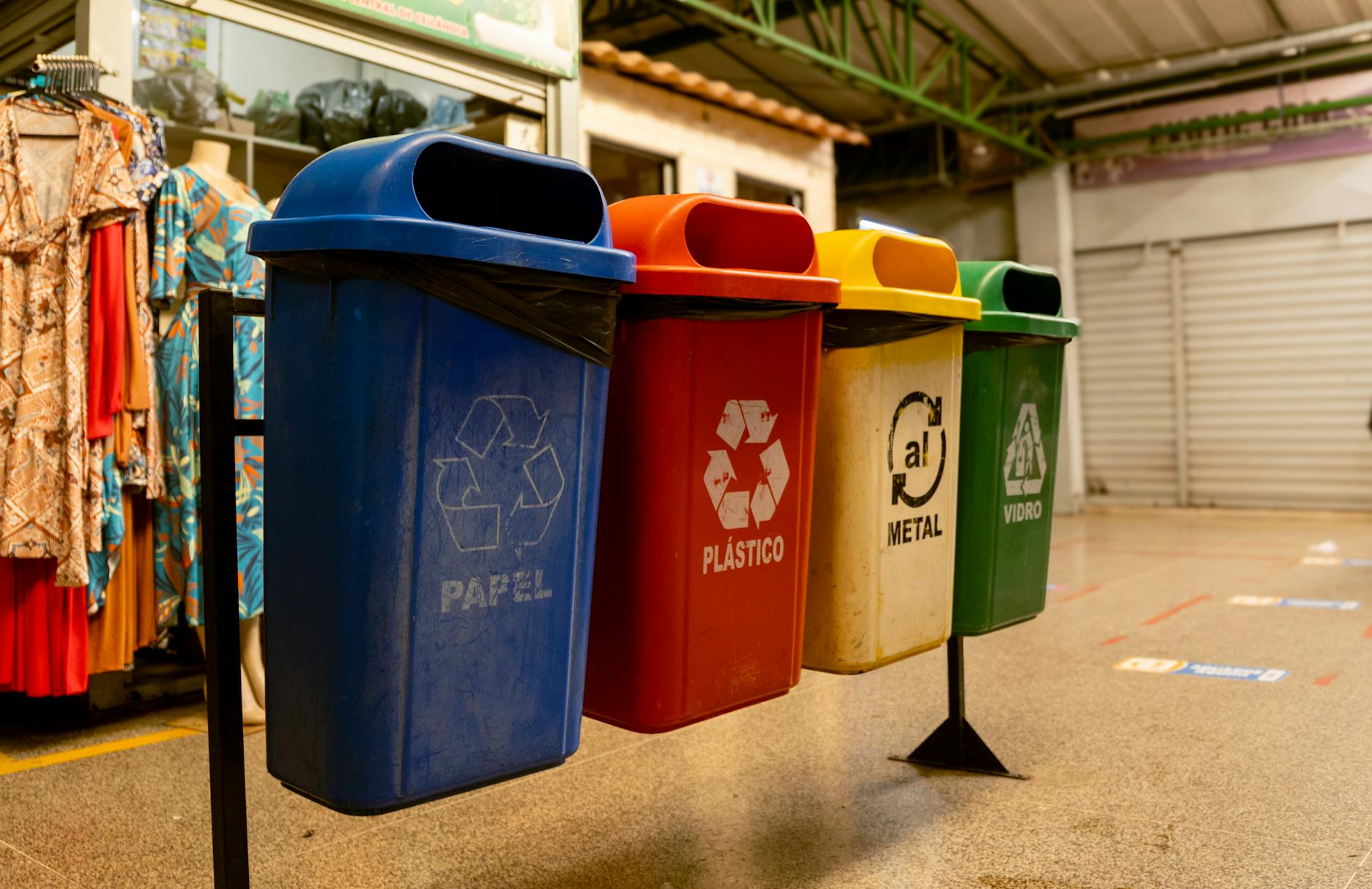 Four recycling bins for paper, plastic, metal, and glass indoors.