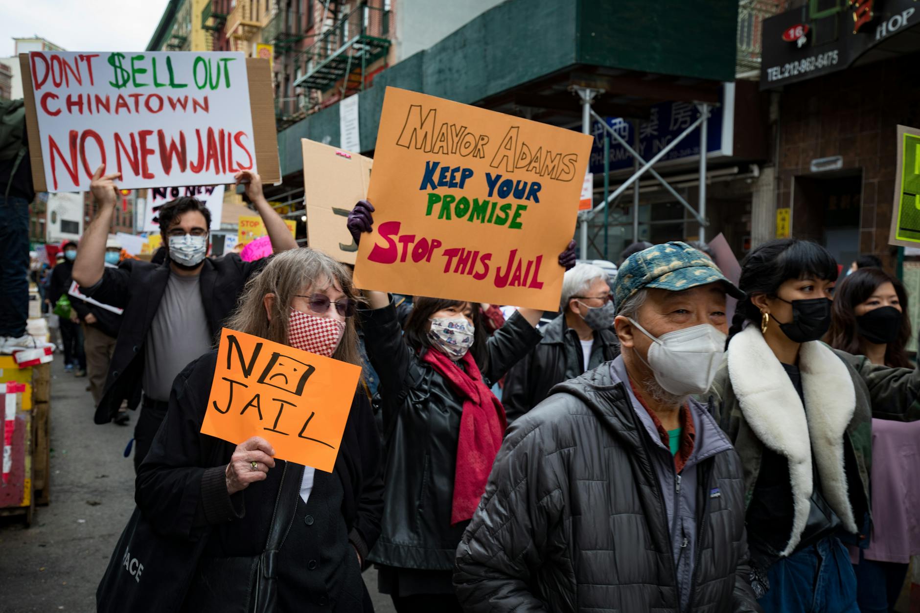 Protesters rally in Chinatown NYC against new jail plans, holding signs and placards.